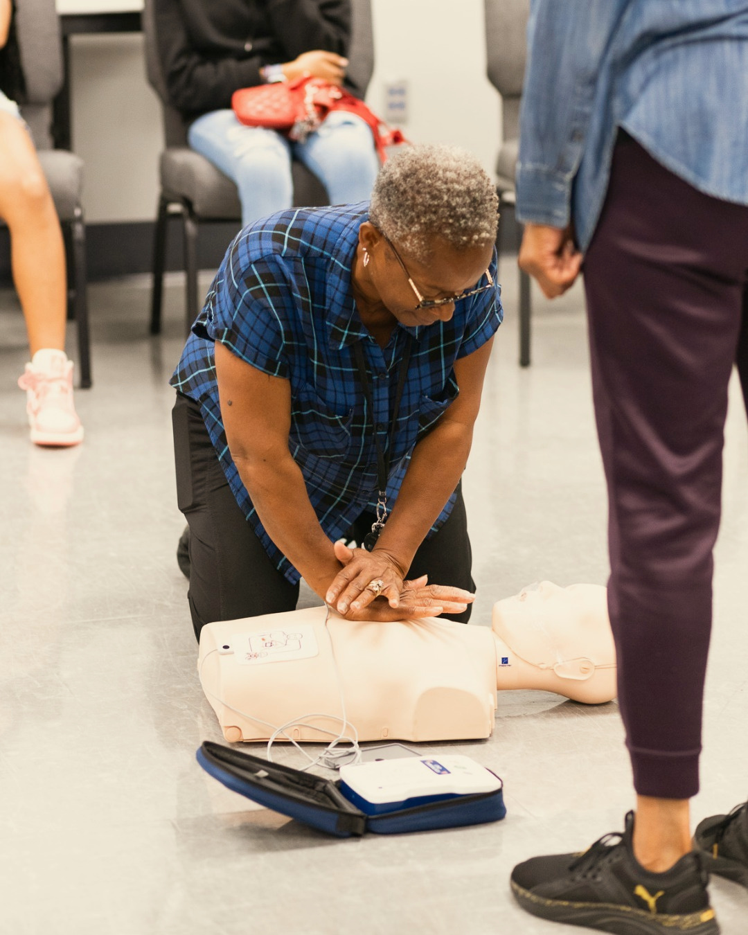 A community participant practices CPR compressions beside an AED trainer